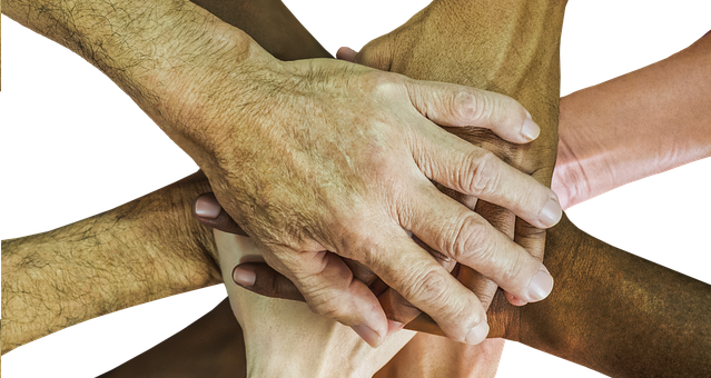 hands of people of different colours, the hands are laid on top of each other.