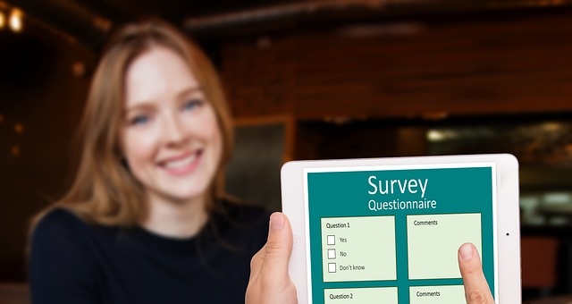 A woman smiling, in the foreground are hands holding a mobile device with a survey
                 displayed on the screen.